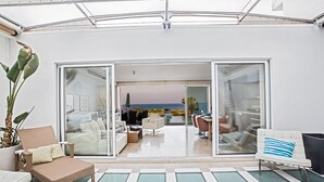A spacious indoor area with a view of the ocean, featuring a seating area with a sofa and chairs, a dining table, and a large potted plant. - Luxury 5 Bedroom Villa with Private Pool, Protaras Villa 1272 (Protaras)