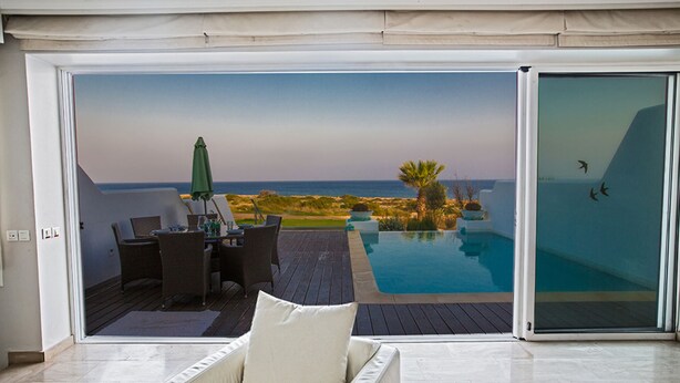 A modern outdoor living area with a pool, dining setup, and a view of the ocean. - Luxury 5 Bedroom Villa with Private Pool, Protaras Villa 1272 (Protaras)