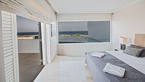 A modern bedroom with a large bed, a view of the beach, and a sliding door leading to an outdoor area. - Luxury 5 Bedroom Villa with Private Pool, Protaras Villa 1272 (Protaras)
