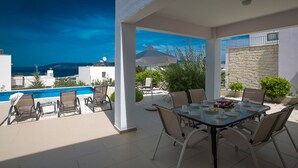 En terrass med pool, utomhusmöbler och utsikt över havet.