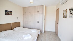 A bedroom with two beds, a wardrobe, and a door. - Picture This (Ayia Napa)