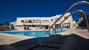 A swimming pool with lounge chairs and a building with multiple balconies in the background. - Picture This (Ayia Napa)