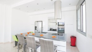 A modern kitchen with a central island, stainless steel appliances, and a red trash bin. - Luxury 5 Bedroom Villa with Private Pool, Protaras Villa 1230 (Protaras)