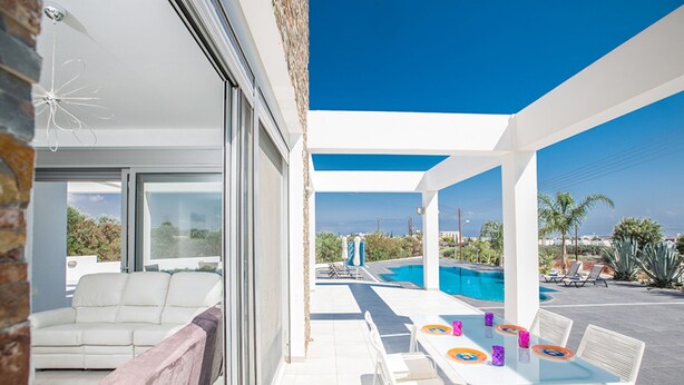 A modern outdoor living space with a pool, white furniture, and a view of the ocean. - Luxury 5 Bedroom Villa with Private Pool, Protaras Villa 1230 (Protaras)