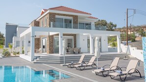 A modern two-story house with a swimming pool, outdoor seating, and a stone facade. - Luxury 5 Bedroom Villa with Private Pool, Protaras Villa 1230 (Protaras)