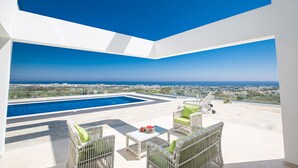 A modern outdoor area with a pool, wicker furniture, and a view of the city and sea.