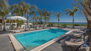 Une piscine rectangulaire bordée de carreaux, entourée de palmiers et de chaises longues.