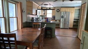 A spacious kitchen with wooden cabinets, a central island, and a dining area with a wooden table and chairs. - Summer And Track Season Rental (Saratoga Springs)