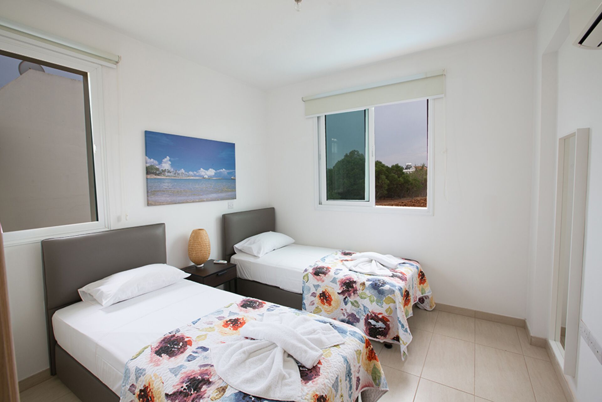 Habitación de hotel con dos camas, una ventana con vista a la playa y un cuadro de una escena costera.