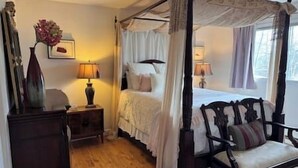 Une chambre à coucher avec un lit à baldaquin, une table de chevet avec une lampe, une chaise et un vase rempli de fleurs.