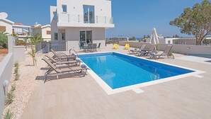 A modern two-story house with a swimming pool, outdoor seating, and a view of the sea. - Luxury 5 Bedroom Villa with Private Pool, Protaras Villa 1250 (Protaras)