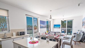 A modern kitchen with a central island, dining area with chairs and a table set for a meal, and a living area with a sofa and a TV. - Luxury 5 Bedroom Villa with Private Pool, Protaras Villa 1250 (Protaras)