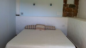 A small, cozy room with a single bed, a plain wall, and a stone wall section. - Green oasis with sea view  (Golfo Aranci)