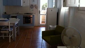 A compact kitchen with blue cabinets, a white refrigerator, and a dining area with a table and chairs. - Green oasis with sea view  (Golfo Aranci)