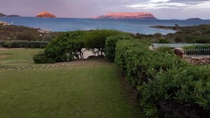 A coastal landscape with a grassy area, dense shrubbery, and a view of the sea and distant islands. - Green oasis with sea view  (Golfo Aranci)