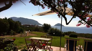 A patio with a table and chairs, a pergola with a canopy, and a view of the sea and mountains. - Green oasis with sea view  (Golfo Aranci)