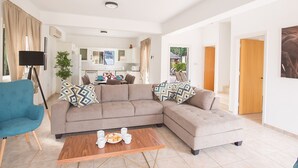 A modern living room with a sectional sofa, a coffee table, and a blue armchair. - How to Rent Your Own Private Luxury Holiday Villa in Protaras for Less than Basic Hotel (Protaras)