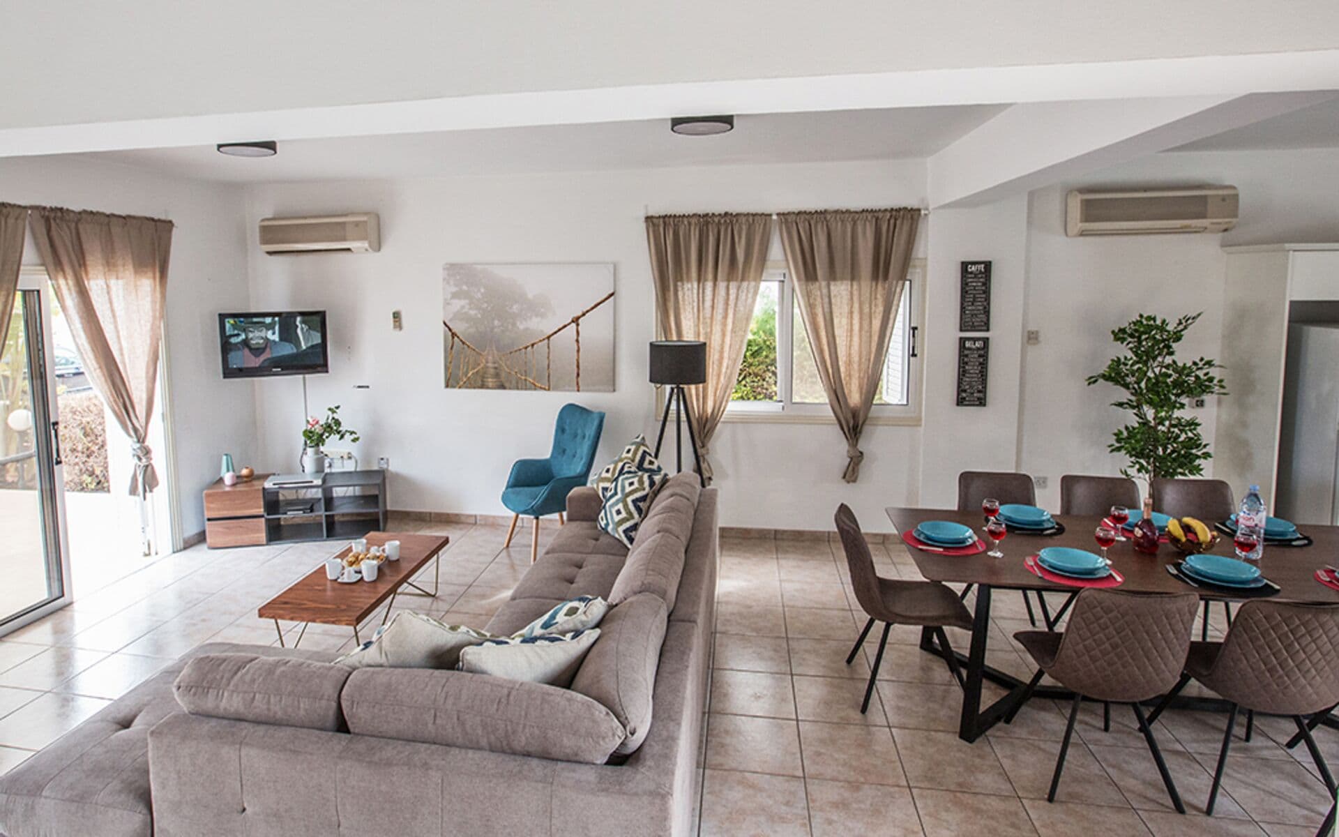 A modern living room with a sofa, a dining table set for four, and a television mounted on the wall.