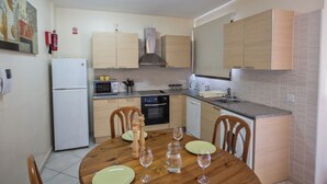 Cocina compacta con una mesa de comedor lista para cuatro personas, equipada con electrodomésticos básicos y salpicadero de azulejos.