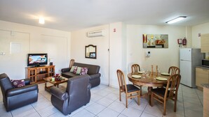 Un salón con sofá, televisión y comedor con mesa dispuesta para cuatro.