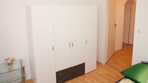 Une pièce avec une grande armoire blanche, une table en verre sur laquelle se trouve un vase, et un coussin vert.