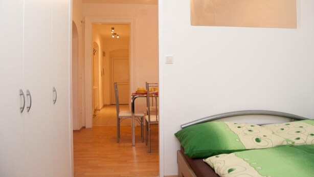 Une chambre à coucher avec un lit, une couverture verte et beige, et une tête de lit en bois.