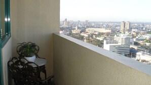 A balcony with a view of a cityscape, a potted plant, and a table with chairs. - 1-BR Robinson Place Residences, 68 sqm. Condo (Ermita Manila)