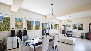 A modern living room with a dining area, large windows, and artwork on the walls.