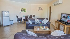 Ein Wohnzimmer mit einer Couch, einem Couchtisch, einem Fernseher und einem Essbereich mit Stühlen und einem Tisch.