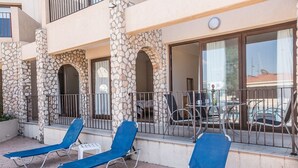 Ein Gebäude mit einer steinernen Fassade, einem Balkon mit blauen Lounge-Stühlen und einem Tisch mit Stühlen.