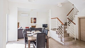Ett rymligt vardagsrum med ett matbord, stolar, en soffa, en TV och en trappa.