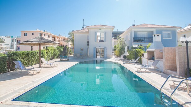 Ein Swimmingpool mit Liegestühlen, einer überdachten Sitzgelegenheit und einem Gebäude mit Balkon.