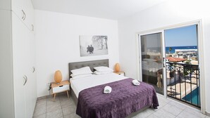 Ein Hotelzimmer mit Bett, Nachttisch, Nachttischlampe, einem Bild an der Wand und einem Balkon mit Meerblick.