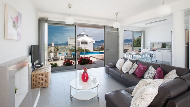 A modern living room with a sofa, coffee table, and a view of a pool and mountains. - The Complete Guide to Renting Your Exclusive Holiday Villa with Private Pool and Close to the Beach (Paphos)