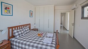 A bedroom with a checkered bedspread, a wooden headboard, a bedside table with a lamp, and a framed picture on the wall. - The Complete Guide to Renting Your Exclusive Holiday Villa with Private Pool and Close to the Beach (Paphos)
