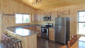Une cuisine aux murs en bois, avec un îlot central doté de tabourets, des appareils électroménagers en acier inoxydable et une fenêtre laissant entrer la lumière naturelle.