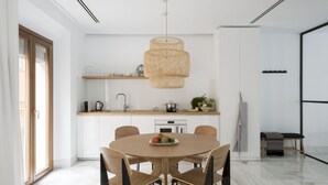 A modern kitchen with white cabinetry, a round wooden dining table, and a hanging rattan light fixture. - Design apartment (Sevilla)