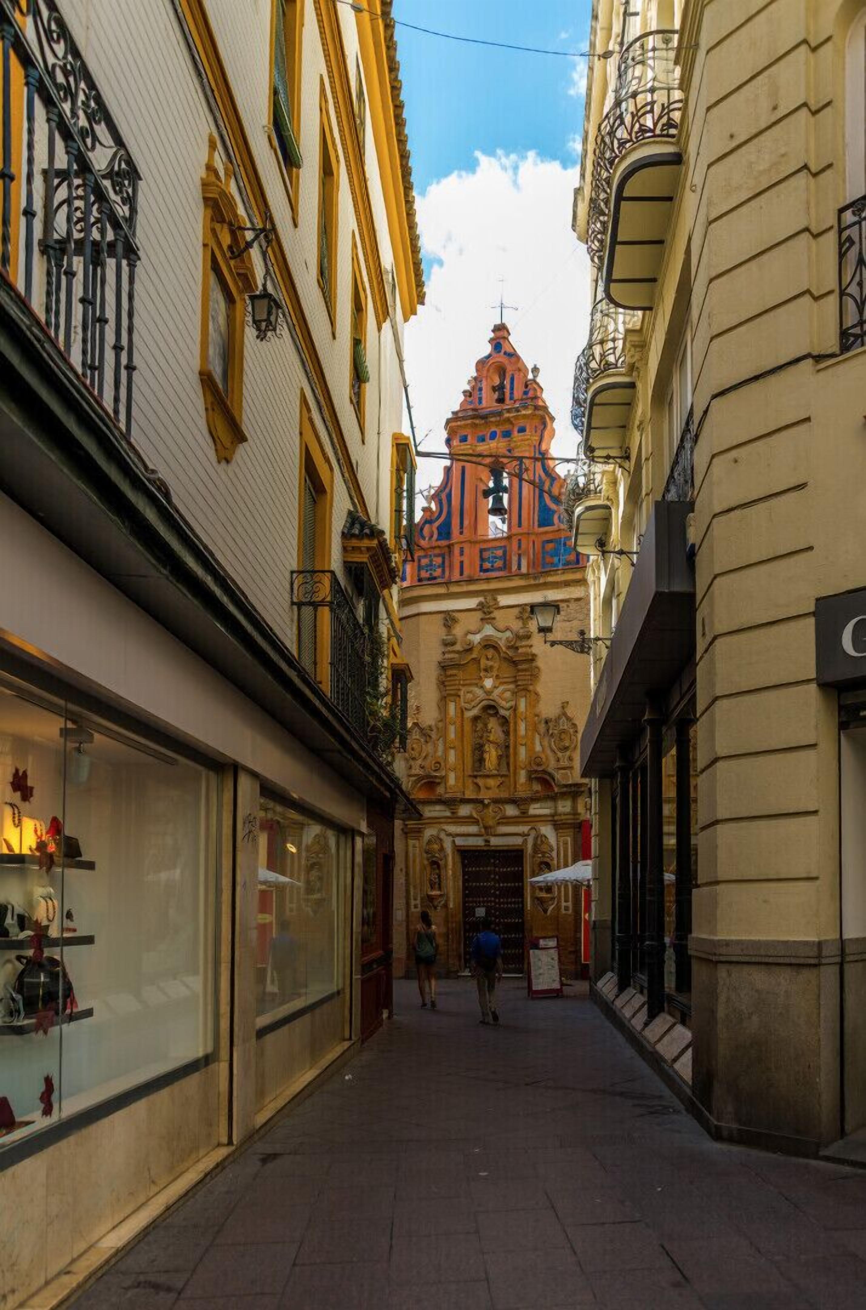 Una stretta via fiancheggiata da edifici decorati, una chiesa in evidenza con una facciata colorata e una persona che passeggia lungo la strada.