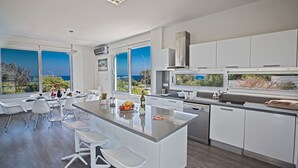 Eine moderne Küche mit einer zentralen Kochinsel, weißen Schränken und großen Fenstern mit Blick auf das Meer.