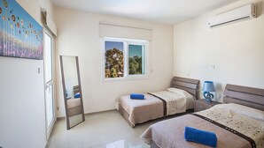 Une chambre avec deux lits simples, un grand miroir, une fenêtre donnant sur des arbres et un appareil de climatisation.
