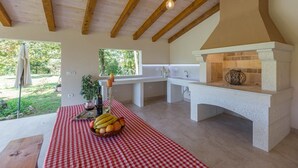 Une cuisine avec un four en pierre, une nappe à carreaux et un panier de fruits.