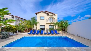 A two-story building with a swimming pool, blue lounge chairs, and palm trees. - Luxury Family Villa Near Protaras Attractions – Protaras Villa 1193 (Protaras)