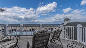 Ein Balkon mit Glastisch und Stühlen, der auf einen Strand und das Meer blickt.