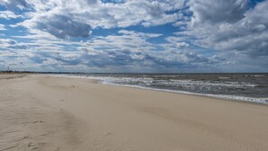 Ein weiter Sandstrand mit sanften Wellen und einem teils bewölkten Himmel.