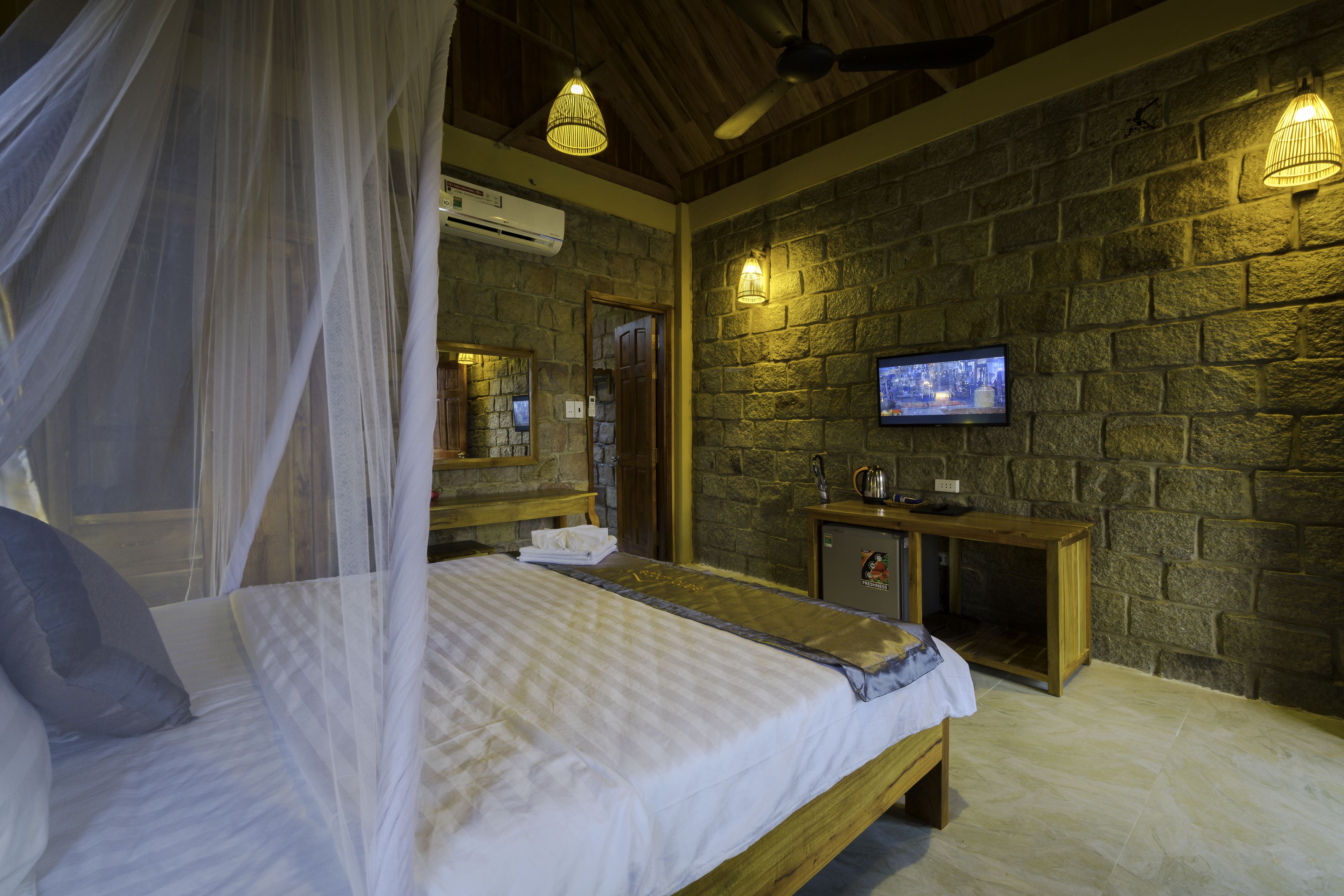 A bedroom with a bed, a television, a stone wall, and a wooden cabinet.