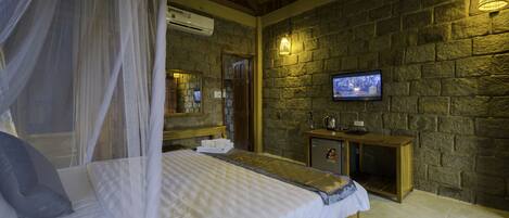 A bedroom with a bed, a television, a stone wall, and a wooden cabinet.