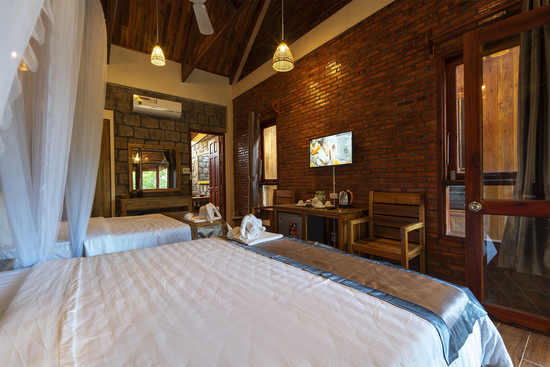 A hotel room with two beds, a stone wall, a wooden ceiling, and a TV on the wall.