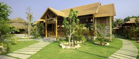 A resort with a thatched-roof building, a covered patio, and a well-maintained lawn with stone pathways.