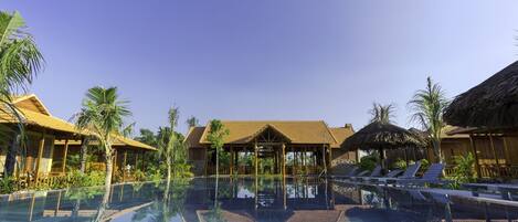 A clear pool with lounge chairs and thatched-roof structures.