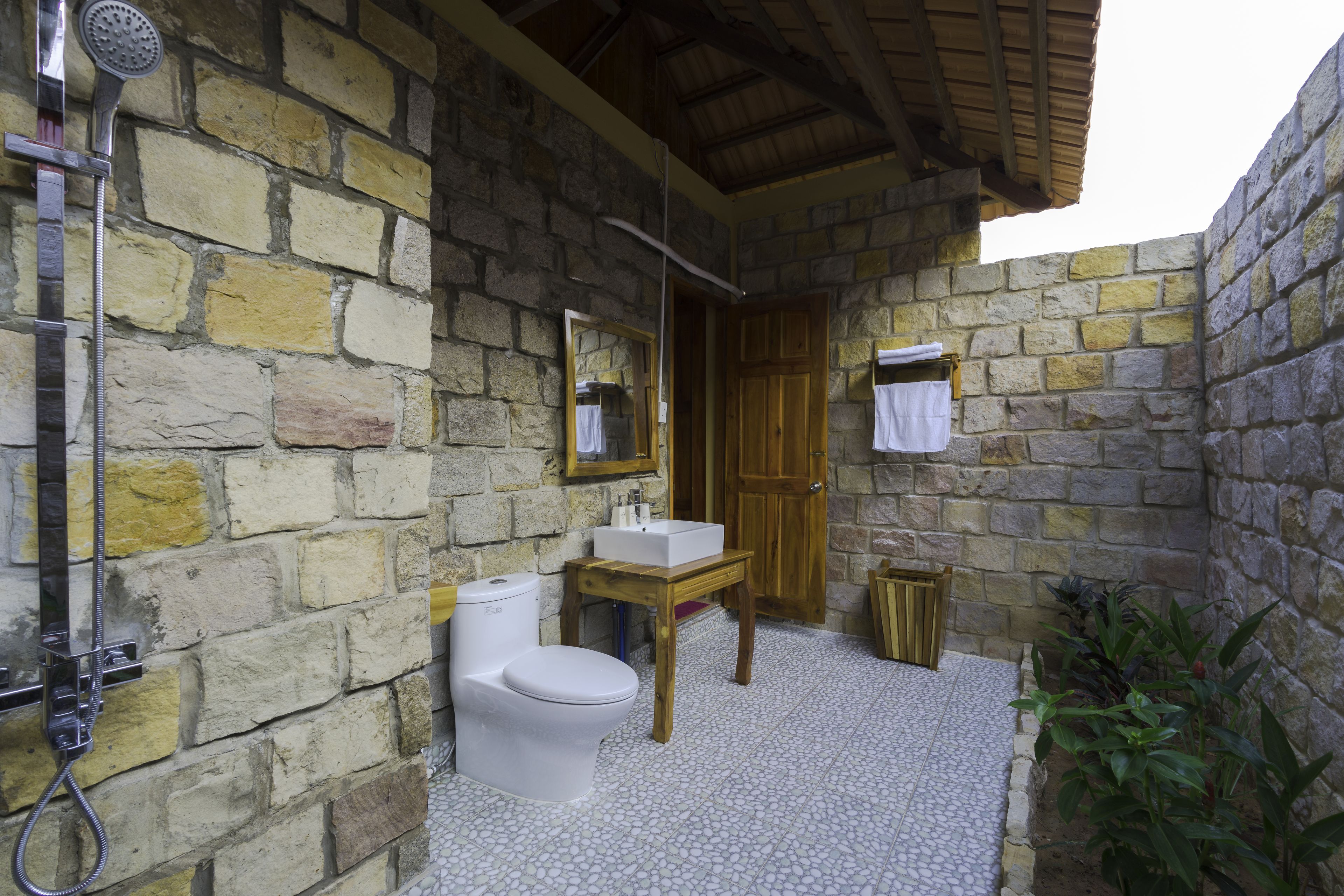 A stone-walled bathroom with a wooden bench, a sink, and a toilet.